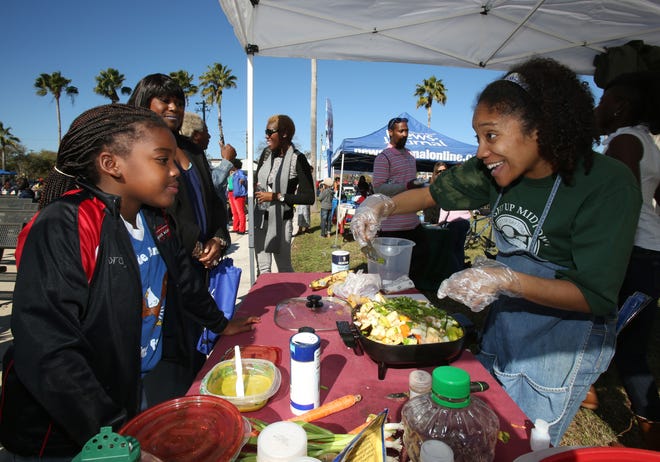 Camille Holder-Brown, right, shows Jordyn Williams, 8, how to prepare vegetables given by Farm Share during Light Up Midtown in Daytona Beach on Saturday.