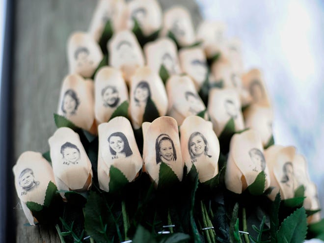 In this Jan. 14, 2013, photo, White roses with the faces of victims of the Sandy Hook Elementary School shooting are attached to a telephone pole near the school on the one-month anniversary of the shooting that left 26 dead in Newtown, Conn. The families of nine of the 26 people killed and a teacher injured two years ago at the school filed a lawsuit against the manufacturer, distributor and seller of the rifle used in the shooting.