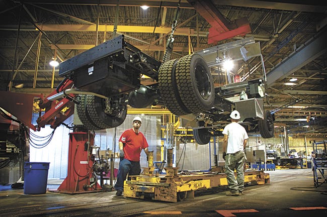 Morgan Olson employees lower a truck chassis to the conveyor system.