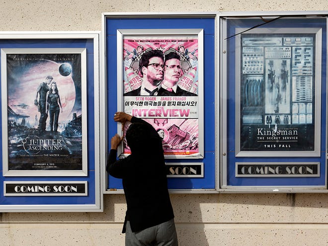 In this Wednesday, Dec. 17, 2014 file photo, a worker removes poster for the movie "The Interview" from a display case at a Carmike Cinemas movie theater in Atlanta. The Alamo Drafthouse in Texas and Atlanta's Plaza Theater on Tuesday, Dec. 23, 2014 said they will begin showing "The Interview" on Christmas Day.