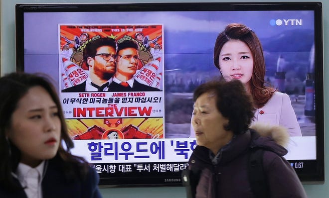 People walk past a TV screen showing a poster of Sony Picture's "The Interview" in a news report, at the Seoul Railway Station in Seoul, South Korea, Monday, Dec. 22, 2014.