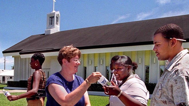 Pastor Carmen Arnett passes out bottles of water to a group of students outside Lakeside United Methodist Church in July 2001.
