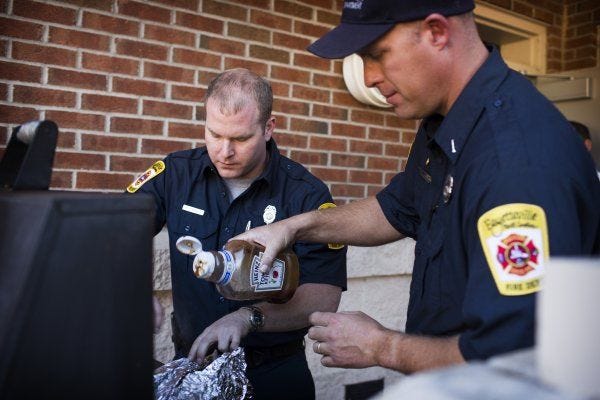 Firefighters Adam Carrier, left, and Lt. Chad Autry pour barbecue sauce over pork on a grill for a family dinner at Fayetteville Fire Department Station 14. Because many firefighters have to work Christmas Day, they invite their families to the station to dine together.