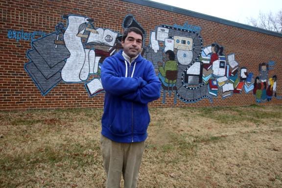 Todd Yelton poses in front of the mural he painted on the Cleveland County Memorial Library to celebrate the library's 100th anniversary. (Ben Earp/The Star)