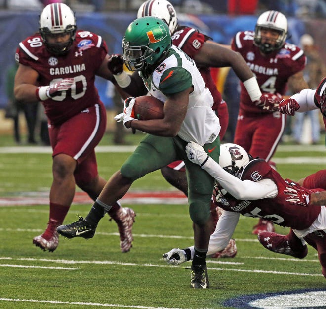 Miami running back Duke Johnson (8) breaks away Saturday from a tackle attempt by South Carolina safety Kadetrix Marcus in the first half of the Independence Bowl NCAA college football game in Shreveport, La.