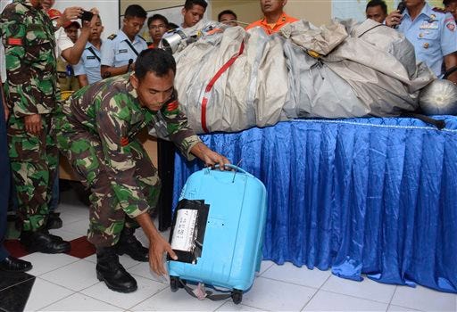 An Indonesian Air Force personnel show a suitcase and airplane parts, on the table, recovered from the water near the site where AirAsia Flight 8501 disappeared, during a press conference at the airbase in Pangkalan Bun, Central Borneo, Indonesia, Tuesday, Dec. 30, 2014.