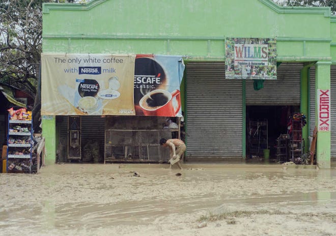 A resident clears the mud off outside his business on Tuesday at Alcantara township, Cebu province in central PhilippinesFruhlein Econar/AP