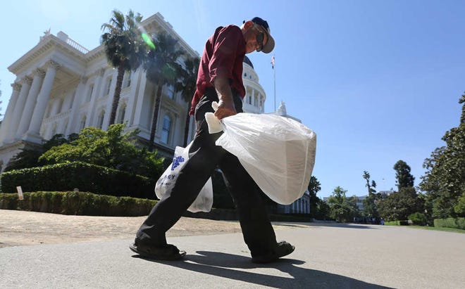 FILE - In this Aug. 12, 2014 file photo, a man carries plastic single-use bags past the State Capitol in Sacramento, Calif. Starting in July 2015, California will become the first state to ban single-use plastic bags under a new law passed by the Legislature and signed by Gov. Jerry Brown in 2014. More than 900 new laws are to take effect in 2015. (AP Photo/Rich Pedroncelli,file)