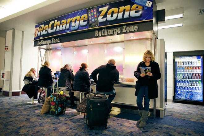 In this Dec. 29, 2014, photo, people use a charging station at McCarran International Airport in Las Vegas. By the end of the annual International CES show a couple thousand outlets and USB ports will be available for those looking for a power charge in Terminal 1 before heading home. (AP Photo/John Locher)