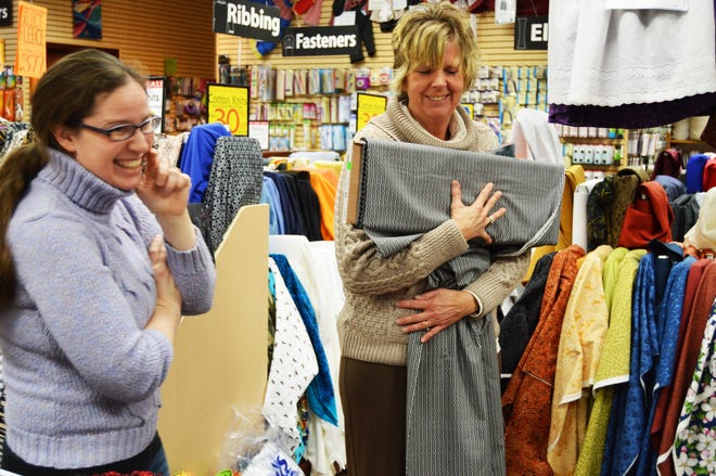 Sharon Zeerip, who works at the Holland Field's Fabric and is the Dutch Dance costume director for Zeeland Schools, holds up a fabric for her counterparts, including Kim Heckman, to consider for costumes while the group met at the store Monday. Annette Manwell/Sentinel staff