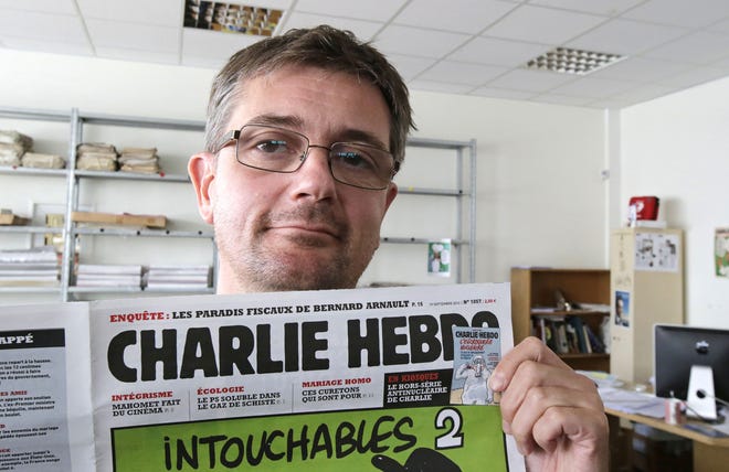 In this Sept. 19, 2012, file photo, Charb, the publishing director of the satyric weekly Charlie Hebdo, displays the front page of the newspaper as he poses for photographers in Paris. Masked gunmen shouting "Allahu akbar!" stormed the Paris offices of a satirical newspaper Wednesday, Jan. 7, 2015, killing 12 people including Charb, before escaping. It was France's deadliest terror attack in at least two decades.