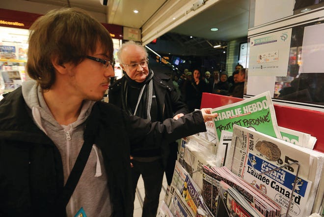 A man picks up a copy of the newspaper Charlie Hebdo at a newsstand in Rennes, France, on Wednesday. In an emotional act of defiance, Charlie Hebdo resurrected its irreverent and often provocative newspaper, featuring a caricature of the Prophet Muhammad on the cover.