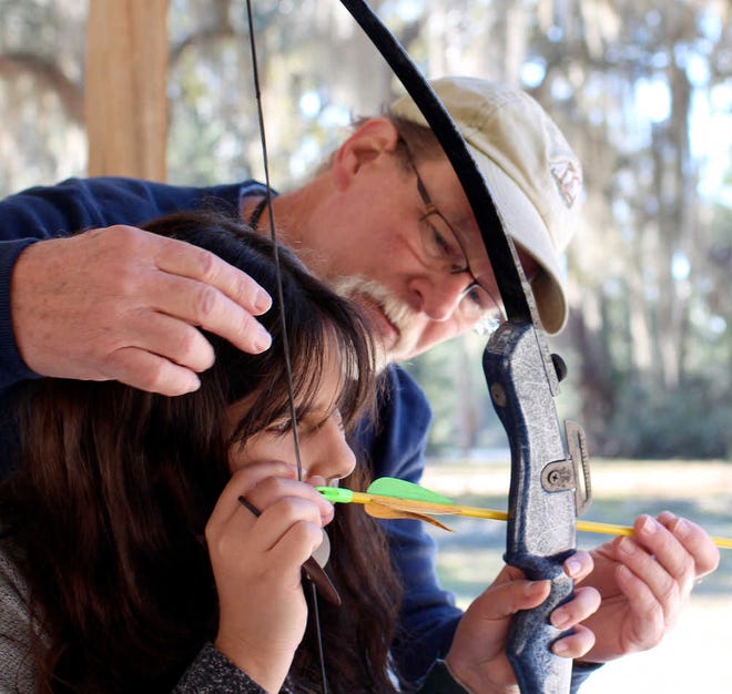 Archery instructor Robert Jones helps visually-impaired Girl Scout Natalie Cruz, of Florida School for the Deaf and the Blind, guide an arrow into place.