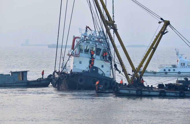 In this photo released by China's Xinhua News Agency, rescuers approach the lifted wreckage of capsized tug boat "Wanshenzhou 67" on the Yangtze River near Jingjiang, east China's Jiangsu Province, Saturday, Jan. 17, 2015. Authorities confirmed 21 people dead in the capsizing of the tugboat with an international team on a test voyage in eastern China, after rescuers dragged the overturned vessel to shallow waters and scoured it Saturday. (AP Photo/Xinhua, Shen Peng) NO SALES