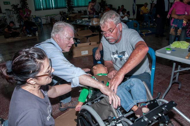 Nick Curtin, another Rotarian and a seating specialist adjust a chair for a young child with cerebral palsy.