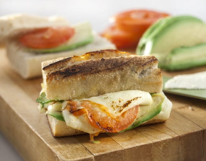 A crusty cheese breakfast sandwich can be adorned with avocado and tomato.