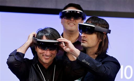 Microsoft's Joe Belfiore, left, smiles as he tries on a "Hololens" device with colleagues Alex Kipman, right, and Terry Myerson following an event demonstrating new features of Windows 10 at the company's headquarters on Wednesday, Jan. 21, 2015, in Redmond, Wash. Executives demonstrated how they said the new Windows is designed to provide a more consistent experience and a common platform for software apps on different devices, from personal computers to tablets, smartphones and even the company's Xbox gaming console. (AP Photo/Elaine Thompson)