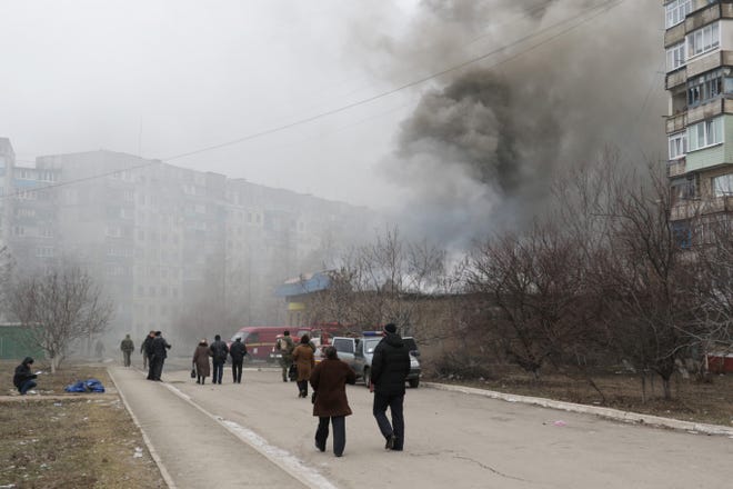 Residents pass by burning houses, a dead body in the background, in Mariupol, Ukraine, Saturday, Jan. 24, 2015. A crowded open-air market in Ukraine's strategically important coastal city of Mariupol came under rocket fire Saturday morning, killing at least 10 people, regional police said. Heavy fighting in the region in the autumn raised fears that Russian-backed separatist forces would try to establish a land link between Russia and Crimea. Pro-Russian separatist forces have positions within 10 kilometers (six miles) from Mariupol's eastern outskirts.