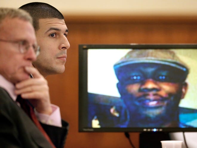 Former New England Patriots and Florida Gators football player Aaron Hernandez, center, listens during his murder trial, Thursday in Fall River, Mass., as defense attorney Charles Rankin, left, looks on while an image of homicide victim Odin Lloyd is displayed on a monitor.