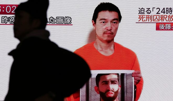 A man walks by a screen showing TV news reports of a YouTube posted by a militant group on Jan. 27, purportedly showing a still photo of Japanese hostage Kenji Goto holding what appears to be a photo of Jordanian pilot Lt. Muath al-Kaseasbeh.