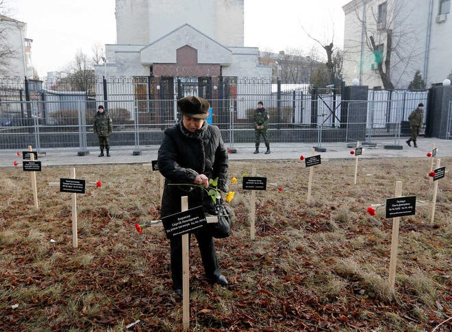 Sergei Chuzavkov/The Associated PressA woman places flowers on one of 30 crosses on Sunday placed by activists bearing the names of people who died in shelling in Mariupol on Jan. 24 outside the Russian Embassy.