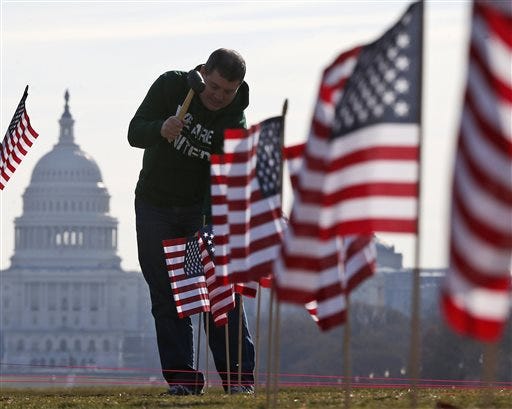 FILE - In this March 27, 2014 file photo, with the Capitol in the background, Army veteran David Dickerson of Oklahoma City, Okla., joins others to place 1,892 flags representing veteran and service members who have died by suicide to date in 2014, on the National Mall in Washington. The Senate is expected to take up a bill Monday named for Clay Hunt, a 26-year-old veteran who killed himself in 2011. The bill is aimed at reducing a suicide epidemic that claims the lives of 22 military veterans every day. (AP Photo/Charles Dharapak)