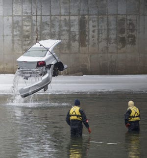 Cherry Valley firefighters watch as a tow truck lifts half of a Dodge Avenger out of the Kishwaukee River on Wednesday, Feb. 11, 2015, near Blackhawk Road in Cherry Valley.