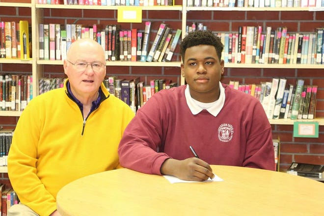 Ascension Catholic head coach Doug Moreau sits next to Delmond Landry after he signed to play football at Southwest Mississippi Community College.