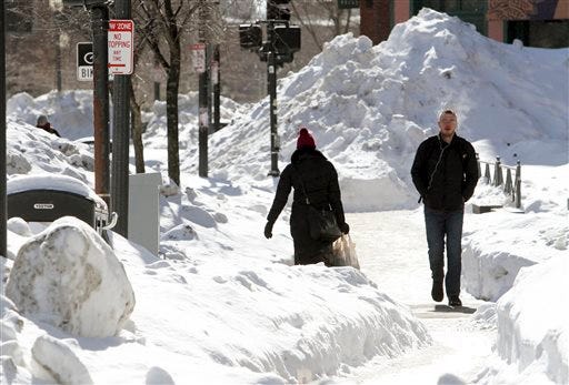 Pedestrians walk among mounds of snow Friday, Feb. 13, 2015, along a street in downtown Boston. Another winter storm that could bring an additional foot or more of snow to some areas is forecast for the region beginning Saturday evening.