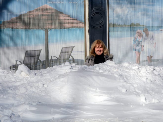 Mary Schonborg, a travel consultant with Whitcomb Travel in Leominster, stands between a snow pile and a warmer image at the agency building.