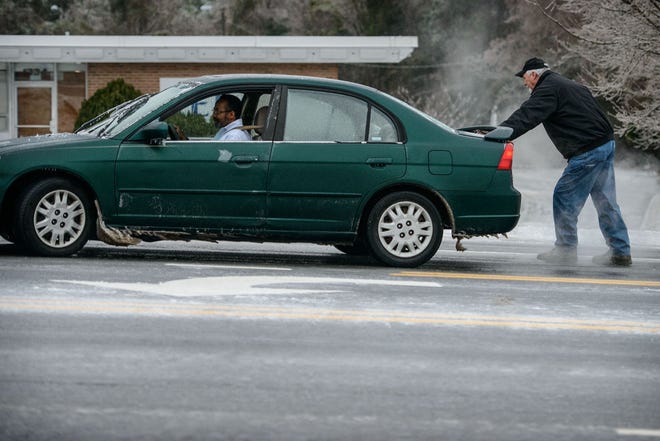 A man helps push a motorist on ice-covered Ramsey Street on Tuesday.