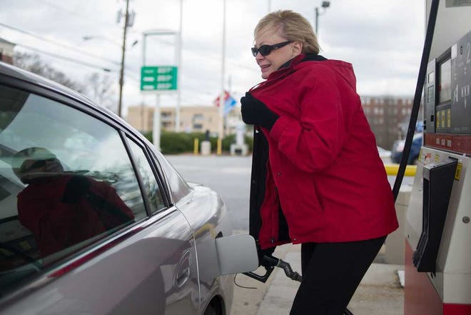 Mary Moore, the house mother at the Kappa Kappa Gamma sorority at the University of Georgia, braces against the cold while pumping gas on Wednesday, Feb. 18, 2015, in Athens,. Ga. Moore said she has been saving money from lower gasoline prices, rather than spending it elsewhere. (AJ Reynolds/Staff, @ajreynoldsphoto)