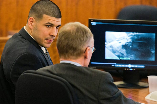 Former NFL player Aaron Hernandez looks at his attorney as security footage is seen on a monitor during his murder trial at the Bristol County Superior Court in Fall River, Mass., Friday, Feb. 20, 2015. Grainy surveillance video shown to jurors in the murder trial of Hernandez on Friday shows the victim an hour before he was killed climbing into a car that prosecutors say was driven by Hernandez. (AP Photo/The Boston Herald, Dominick Reuter)