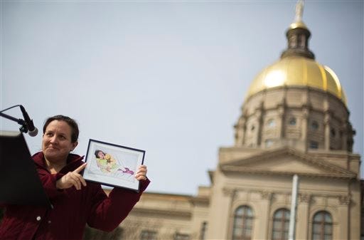 Carrie Hall, of Atlanta, holds up a photo of her daughter Lela, 7, who suffered seizures while living with Dravet Syndrome before passing away Jan. 14 of pneumonia, as she speaks at a rally in front of the Statehouse in favor of House Bill 1, which would legalize possession of cannabis oil for treatment of certain illnesses, Tuesday, Feb. 3, 2015, in Atlanta. Debate has opened on a bill that would legalize the use of cannabis oil for cancer, seizure disorders and other chronic illnesses. A House committee discussed the bill on Tuesday. (AP Photo/David Goldman)