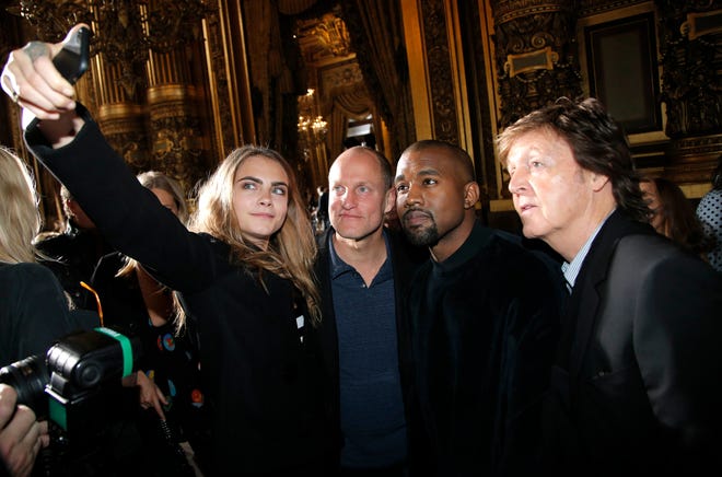 From left, model Cara Delevingne, takes a photographer with actor Woody Harrelson, singers Kanye West and Paul McCartney prior to Stella McCartney's ready to wear fall-winter 2015-2016 fashion collection during Paris Fashion Week, Paris, France, Monday, March 9, 2015. (AP Photo/Thibault Camus)