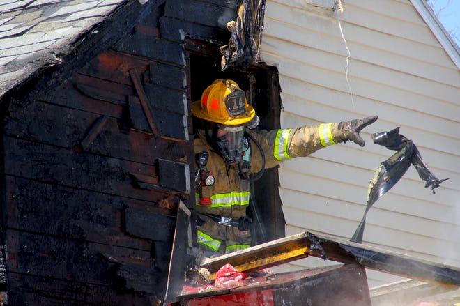 A Dover Firefighter removes a second floor window during a house fire Tuesday at 20 Gerrish Road in Dover.
