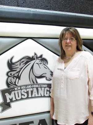 Karen Davison shows her school spirit by standing near the Mustang logo in the New Holland-Middletown Elementary gymnasium. Photo by Jean Ann Miller/The Courier