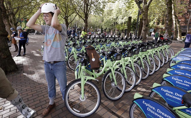 Brock Howell of the Cascade Bicycle Club pulls on a helmet in Seattle as he prepares to lead a ride on the city’s rental bikes. (AP photo/Elaine Thompson)