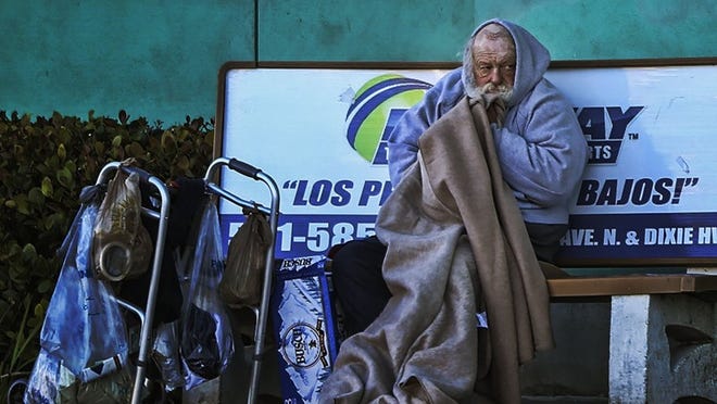 Early Thursday, February 19, 2015, a homeless man who says his friends refer to him as Senator, uses a blanket to shield himself from frigid temperatures on a bench along Dixie Hwy. in Lake Worth adjacent to Publix. “The cold shot right through my bones last night,” said Senator. Forecasts are calling for record lows tonight with the temperature dropping to 37 degrees and winds gusting NW at 10 to 15 mph. (Damon Higgins / The Palm Beach Post)