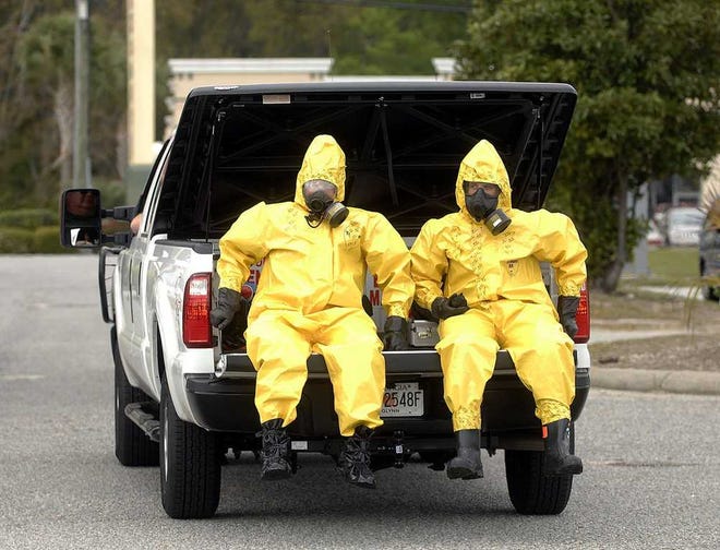 Terry.Dickson@jacksonville.com - 3/30/15 - Glynn County police officers Terry Wright, left, and his son Garrett, ride in the back of a pickukp in hazmat suits as they cross Cypress Mill Road Monday to bring a suspicious package to a decontamination area in a large parking lot across the street. (Florida Times-Union, Terry Dickson)