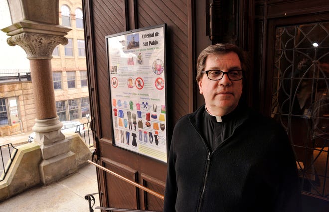 Monsignor Robert K. Johnson stands by one of three posters placed near entrances of the Cathedral of St. Paul, reminding worshipers of appropriate attire and etiquette during Mass.