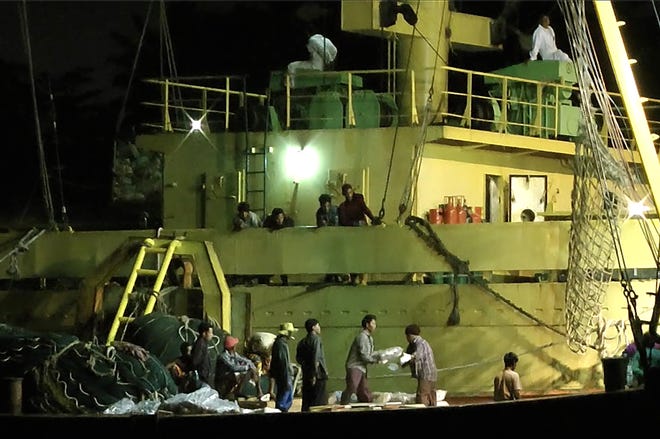 In this Nov. 27, 2014, image from video, workers from Myanmar load fish onto a Thai-flagged cargo ship in Benjina, Indonesia. An intricate web of connections separates the fish we eat from the men who catch it, and obscures a brutal truth: Your seafood may come from slaves.