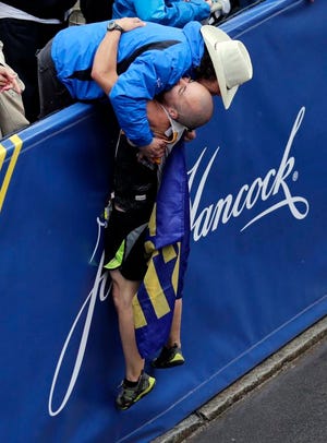 Carlos Arredondo, top, a 2013 Boston Marathon first-responder, hugs Robert Wheeler, of Marshfield also a 2013 first-responder, during a moment of silence at 2:49 p.m., the time of the 2013 bombings, after Wheeler crossed the Boston Marathon finish line, Monday, April 20, 2015, in Boston.