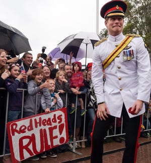 Britain's Prince Harry reacts after shaking hands with kids holding up a sign reading "Red Heads Rule" during a visit to the Australian War Memorial in Canberra, Australia.