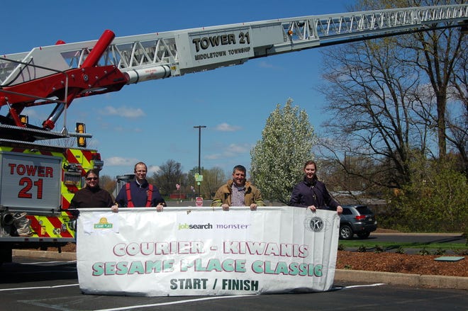 Sesame Place's Heather Goforth (left) and Meghan Ferguson (right) join Langhorne-Middletown Fire Company's Andrew Tomlinson and Chief Frank Farry in getting start/finish banner ready for 17th annual Courier-Kiwanis Sesame Place Classic on May 17.
