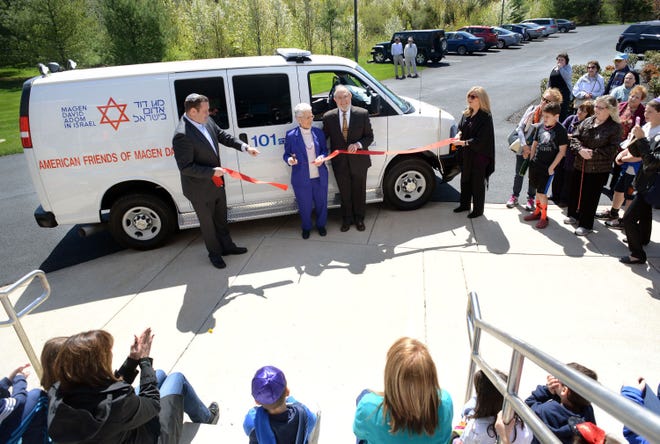 Rabbi Joshua Z. Gruenberg (L) and Sharon Schmidt (R) stand by as a congregation member and donor of the ambulance, who declined to be identified, cut the ribbon at the dedication of an ambulance through the Magen David Adom organization Sunday April 26, 2015 at Congregation Beth El in Lower Makefield, Pennsylvania. (Photo by William Thomas Cain/Cain Images)