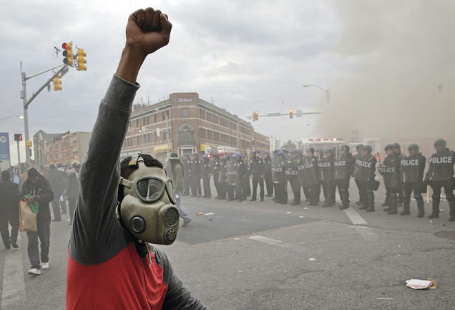 Top, a demonstrator raises his fist as police stand in formation as a store burns Monday during unrest following the funeral of Freddie Gray in Baltimore. Gray died from spinal injuries about a week after he was arrested and transported in a Baltimore Police Department van. Left, Baltimore firefighters battle a three-alarm fire at a senior living facility under construction. It was one of several fires reported amid rioting. Above, a police officer patrols near a blaze Monday evening. Patrick Semansky/Asssociated Press