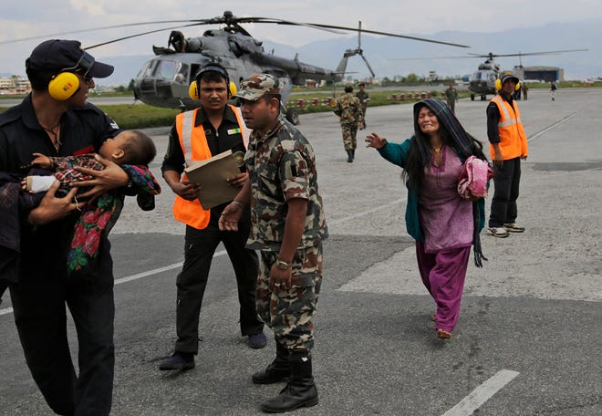 An Indian Air Force person walks carrying a Nepalese child, wounded in Saturday'­s earthquake, to a waiting ambulance as the mother rushes to join after they were evacuated from a remote area at the airport in Kathmandu, Nepal, Monday, April 27, 2015.