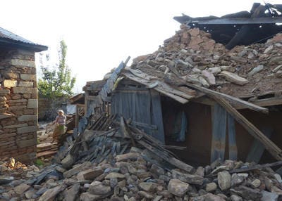 In this Monday, April 27, 2015, photo provided by the International Nepal Fellowship, an elderly woman is seen standing at her collapsed home in the village of Pokhridada, in Gorkha district, about 25 kilometers (15.5 miles) from the epicenter of Saturday's massive earthquake in Nepal. (Thomas Meier/International Nepal Fellowship via AP)