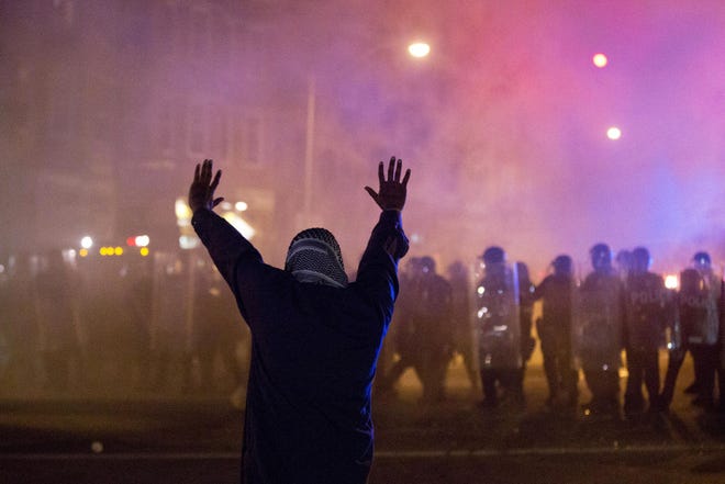 A protester faces police enforcing a curfew Tuesday, April 28, 2015, in Baltimore.